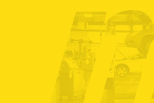 In the shape of an M and overlaid with yellow, two cards are being worked on in a Meineke car care center, one car is jacked up, the other car is ground level